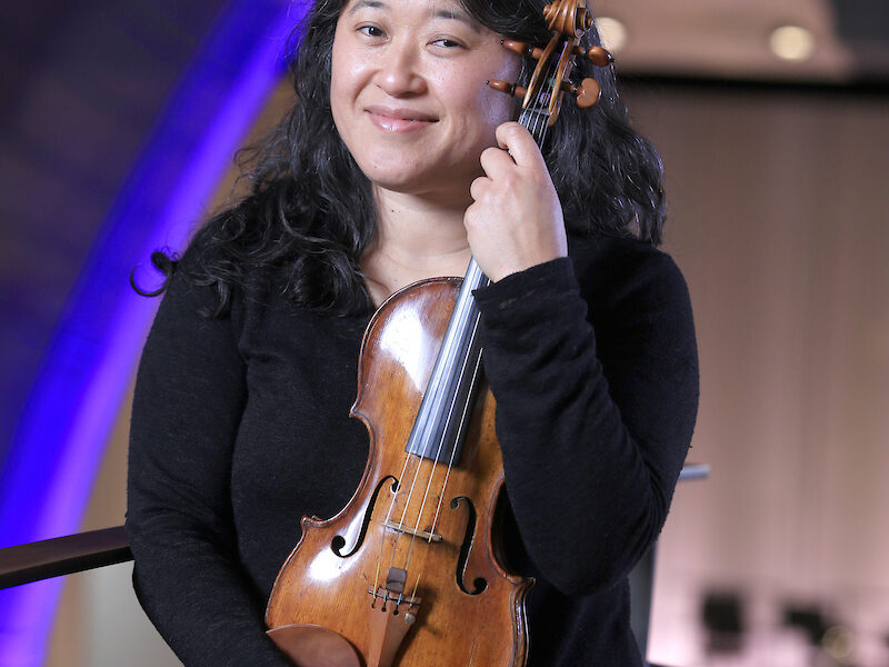 a woman smiles at the camera while holding a violin