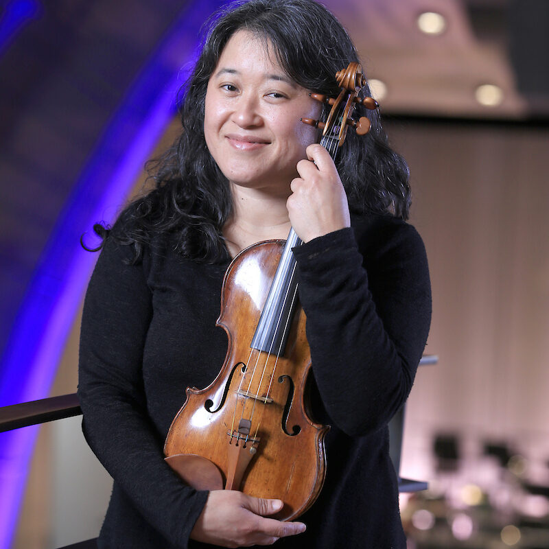 a woman smiles at the camera while holding a violin