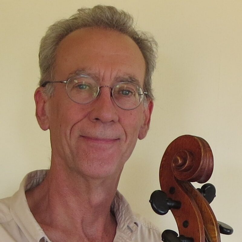A man smiling at the camera with the scroll of a cello next to him