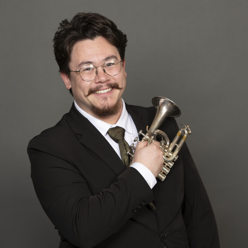 A man holding a trumpet smiles at the camera